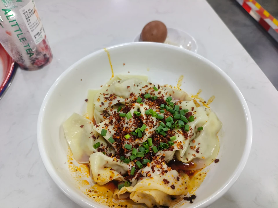 Wontons with scallions and chili in a white bowl